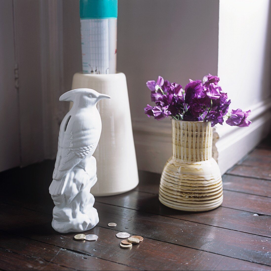 A white bird figurine next to a vase on flowers on a wooden floor