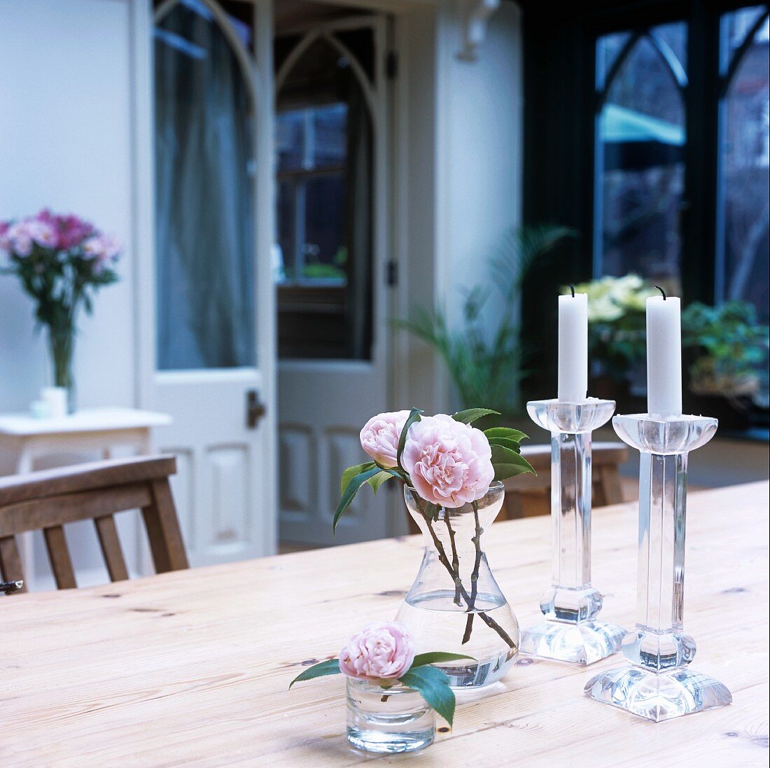 Kleine Glasvasen mit Rosen und Kerzen auf einem Tisch