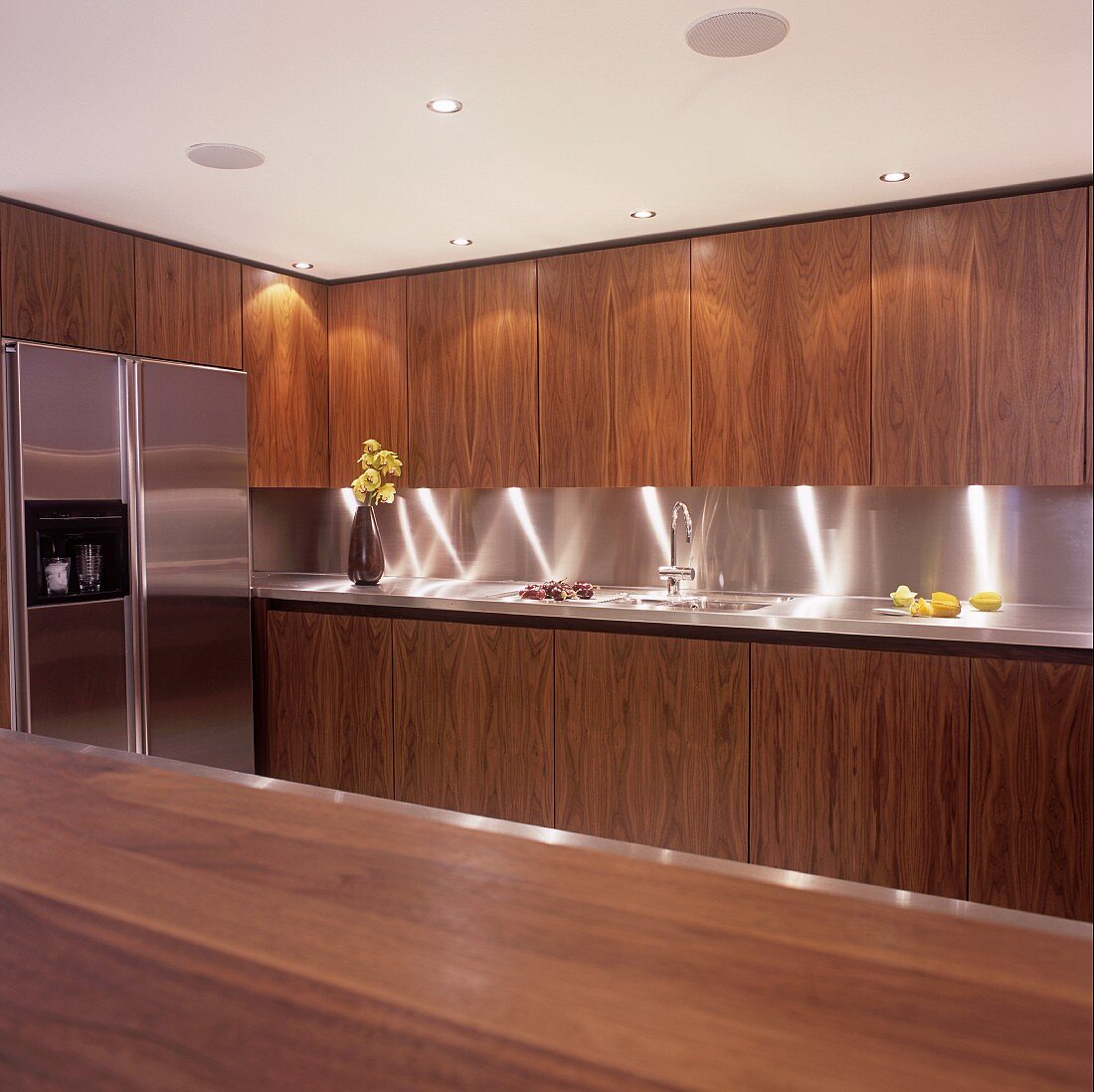 An illuminated kitchen with wooden cupboards and a stainless steel fridge