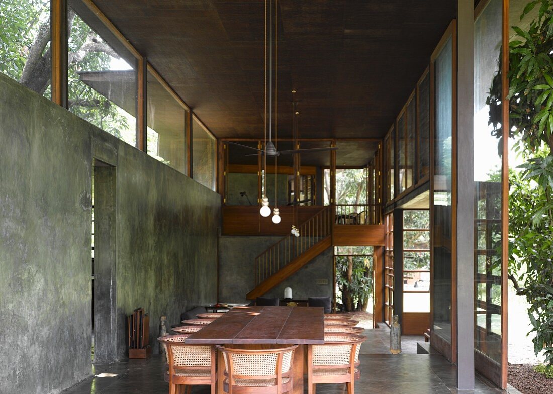 Esstisch mit traditionellen Stühlen und Geflecht in Rückenlehne im zeitgenössischen Wohnraum aus Beton und raumhohen Terrassentüren