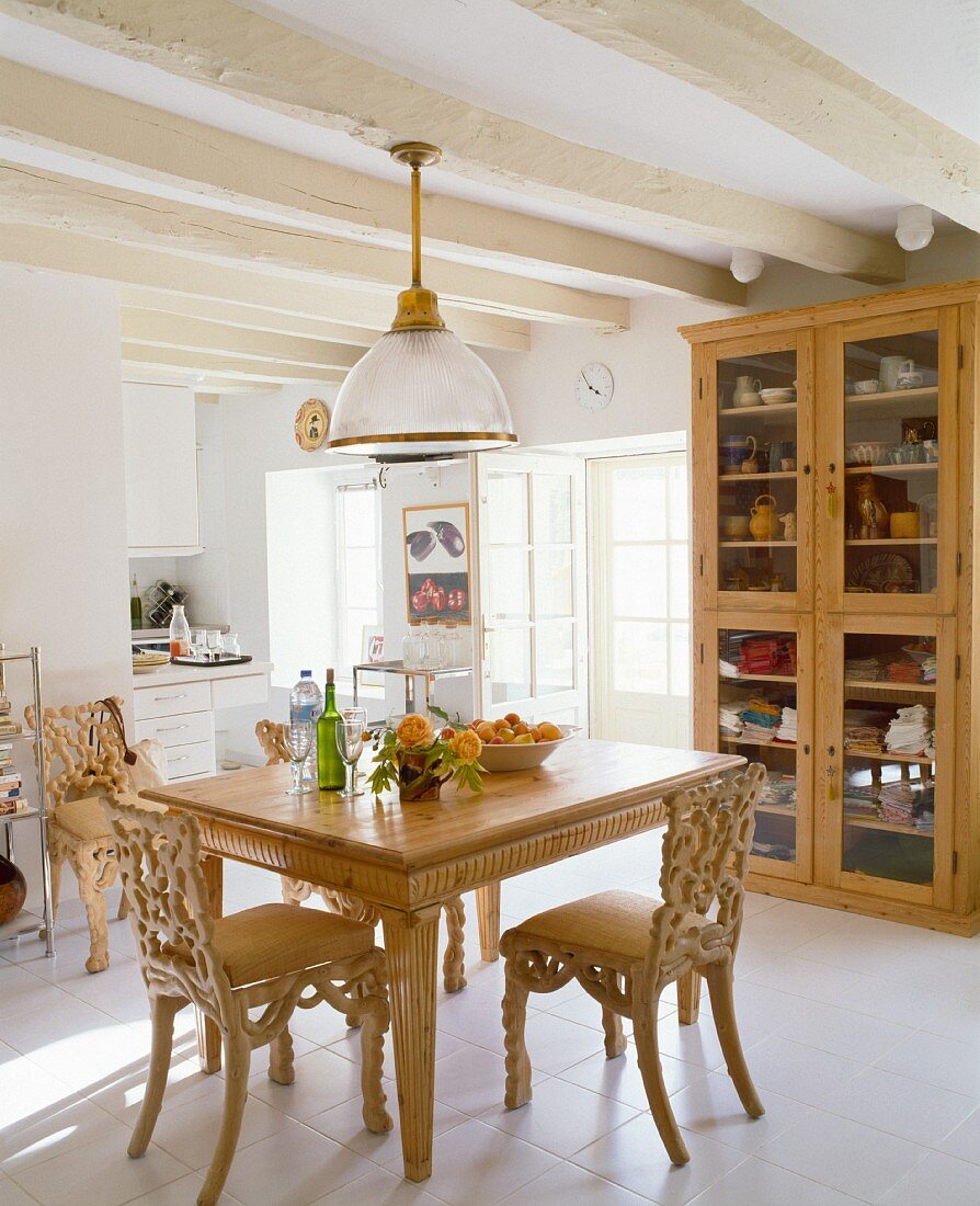 Rustic dining room with carved wooden chairs and table in front of a a glass hutch