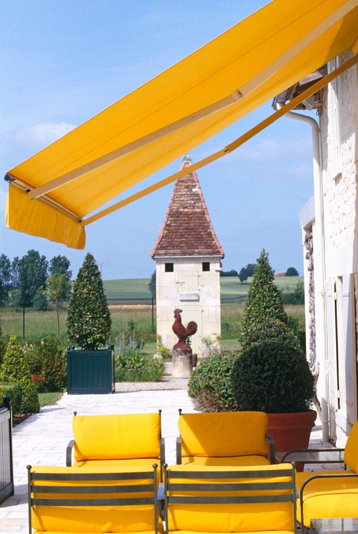 Metallstühle mit gelben Polstern unter gelber Markise auf Terrasse