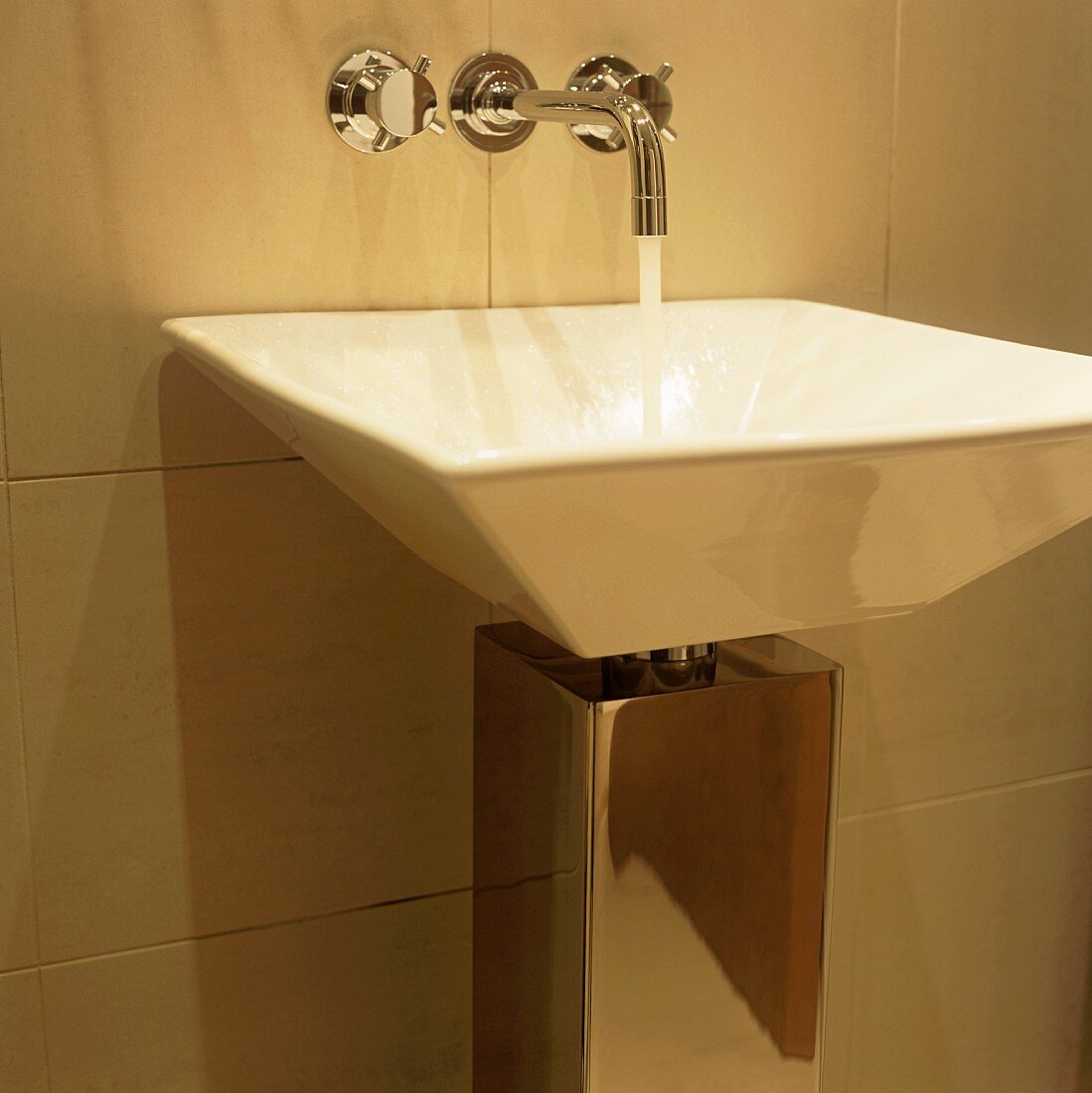 Water running from wall taps into a designer wash basin with chrome cladding around the outlet pipe