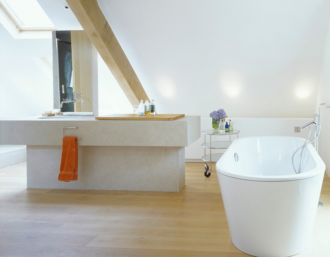 A free-standing bathtub with a designer floor tap and an island counter under a sloping roof