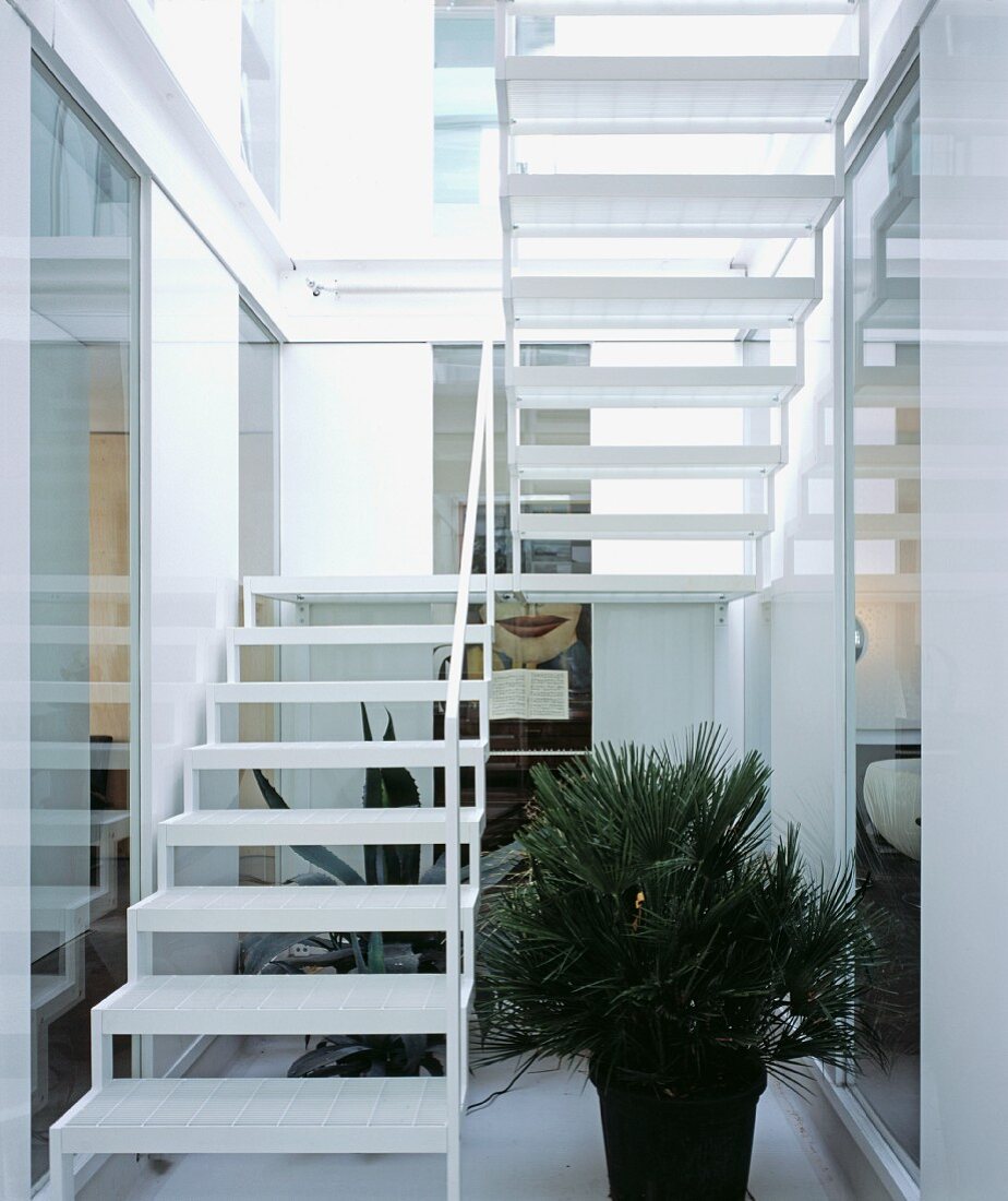 Open-structured, white staircase with slightly transparent treads and plants in stairwell flooded with light