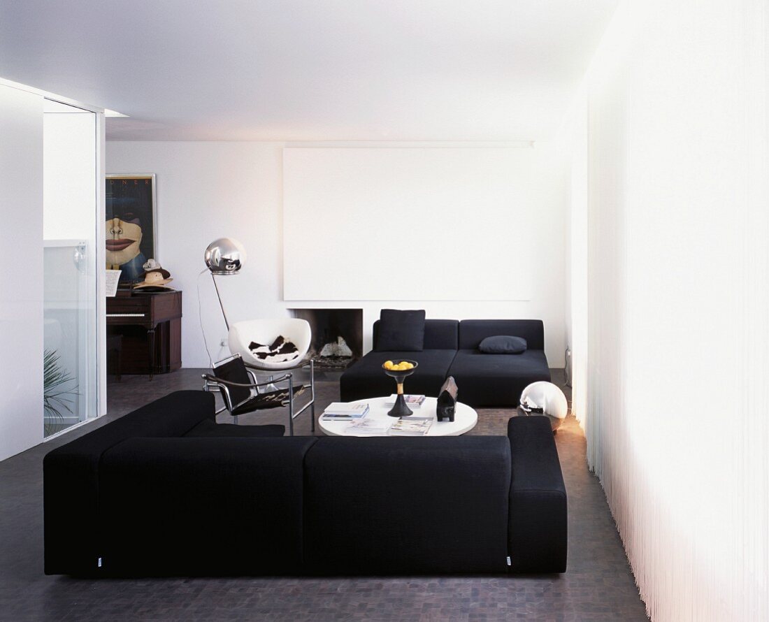 Weisser, moderner Wohnraum mit schwarzer Sofalandschaft auf grauem Boden