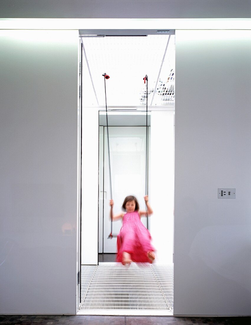 Blurred view through doorway of girl in pink dress on swing in light stairwell