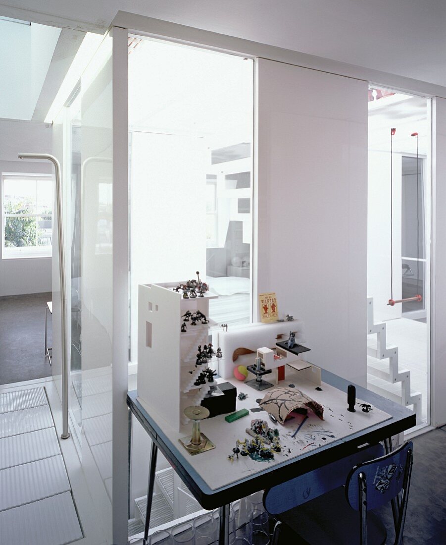 Arbeitstisch mit Architekturmodellen vor raumhohen Fenstern mit Blick in Treppenraum
