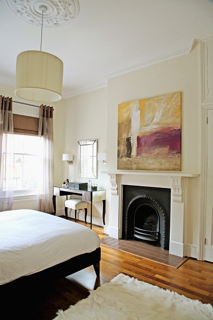 Schlafzimmer mit elegantem Frisiertisch und modernem Gemälde in Altbau mit Stuck und traditionellem Kamin