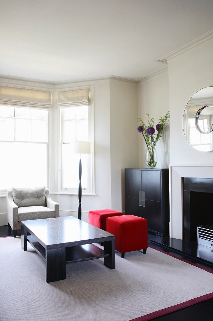 Modernes Wohnzimmer mit schwarzen Holzmöbeln und roten Polsterhockern auf weißem Teppich