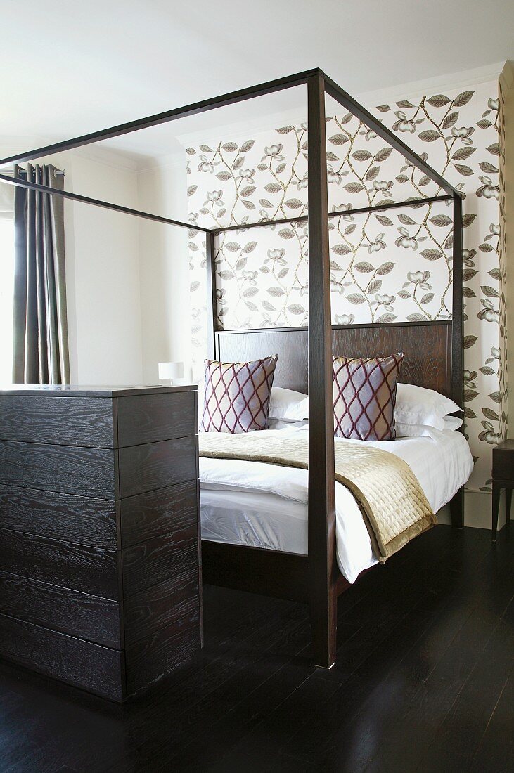Doppelbett mit Himmelgestell und Zierkissen vor Tapete mit floralem Muster in modernem Schlafzimmer