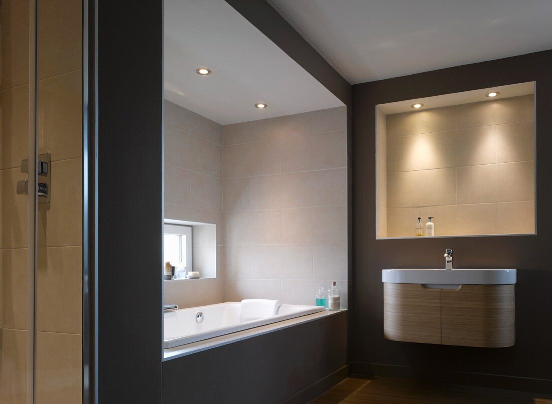 Beleuchtete Wandnische über Designer-Waschtisch und Badewannennische mit Fenster in Bad in warmen Naturfarben