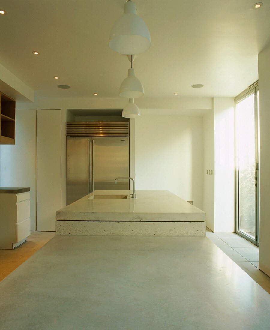 Blick über Küchen-Arbeitsplatten aus Stein mit integriertem Spülbecken auf grossen Edelstahl-Kühlschrank