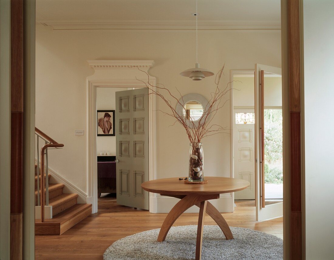 Runder Holztisch mit Viertelkreisrahmen als Tischbeinen auf rundem Teppich im lichten Eingangsbereich eines englischen Wohnhauses