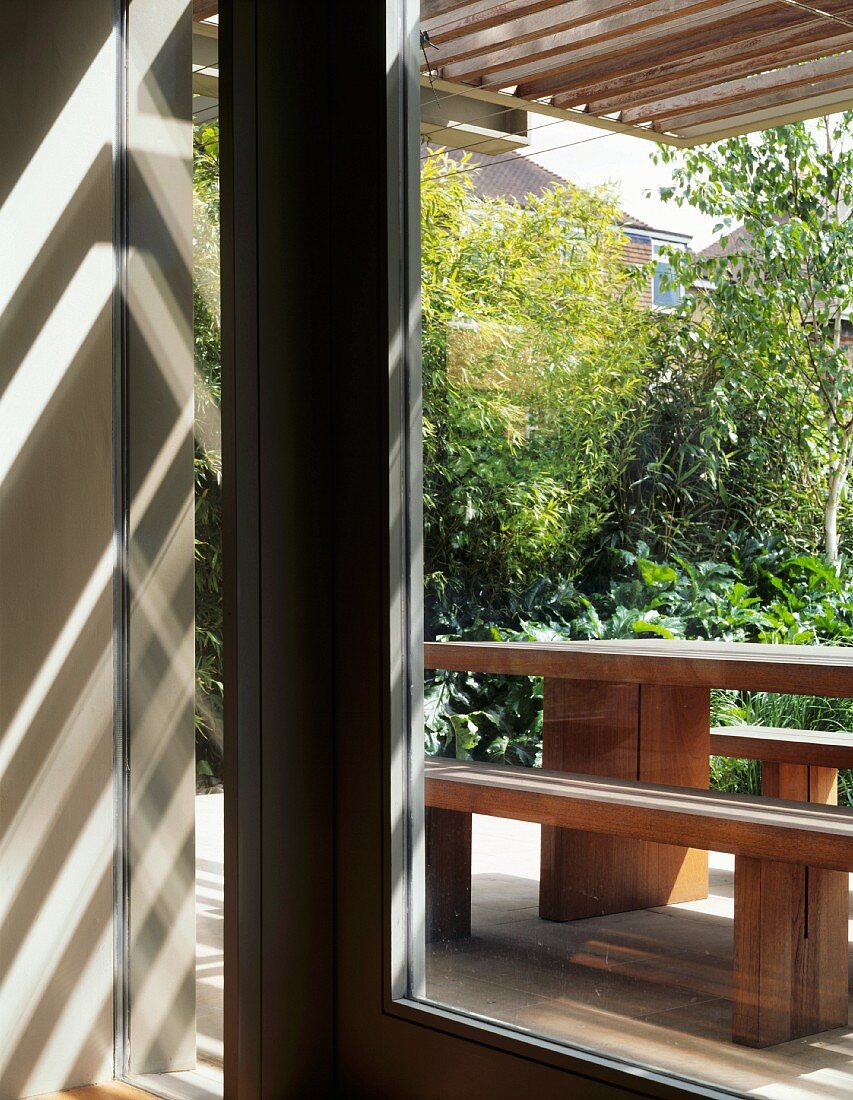 Sonnenstrahlen durch Holzpergola über Gartenterrasse mit einfachem Sitzplatz aus massiven Holzplatten