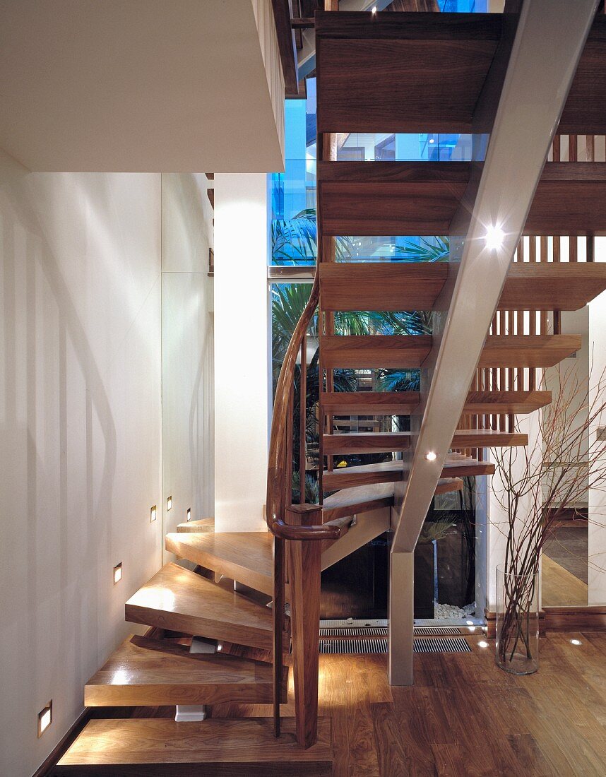 Gewendelte, offene Holztreppe auf mittiger Stahltragkonstruktion vor Fenster im blauen Dämmerlicht