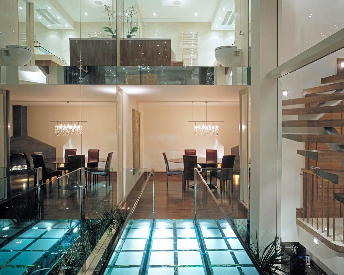 Bridge of illuminated glass bricks with view of rooms between reflective glass panels in English house
