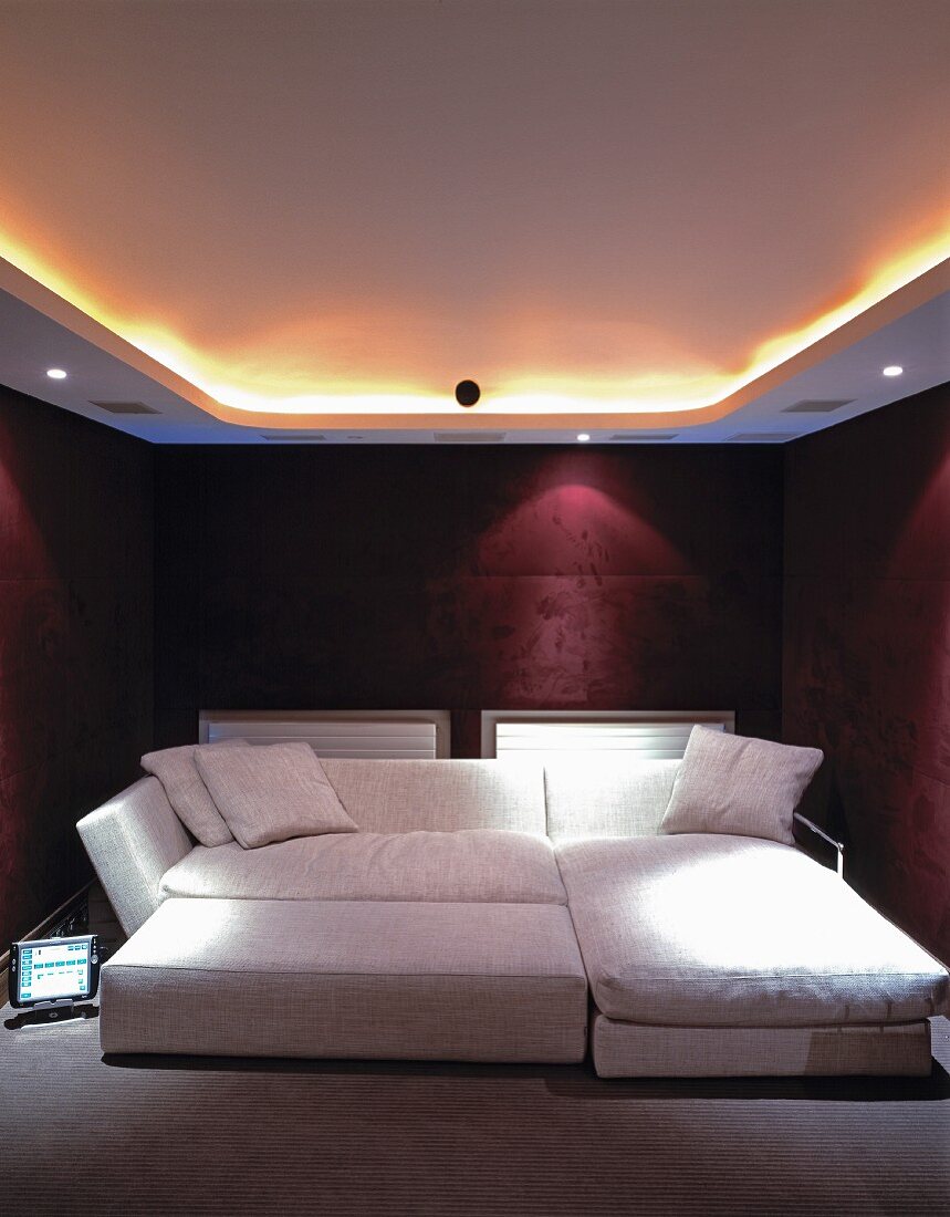 Indirektes Deckenlicht und Spots über breitem Sofabett in bordeaux-farbenem Schlafzimmer