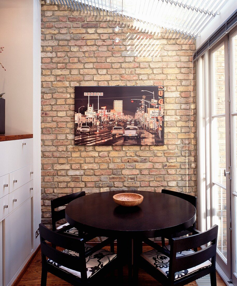 Round, black dining table in conservatory extension with modern photograph on brick wall