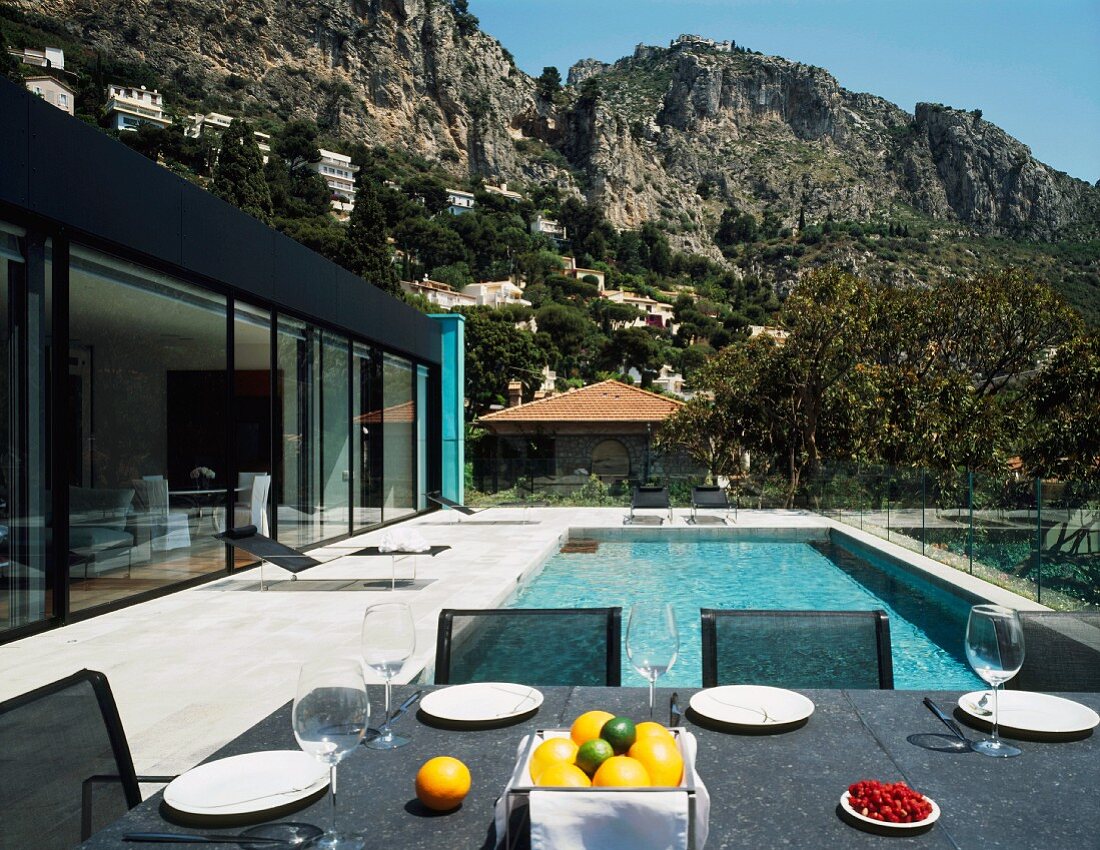 A contemporary house with a view of a rocky landscape with a table laid on a terrace in front of a pool