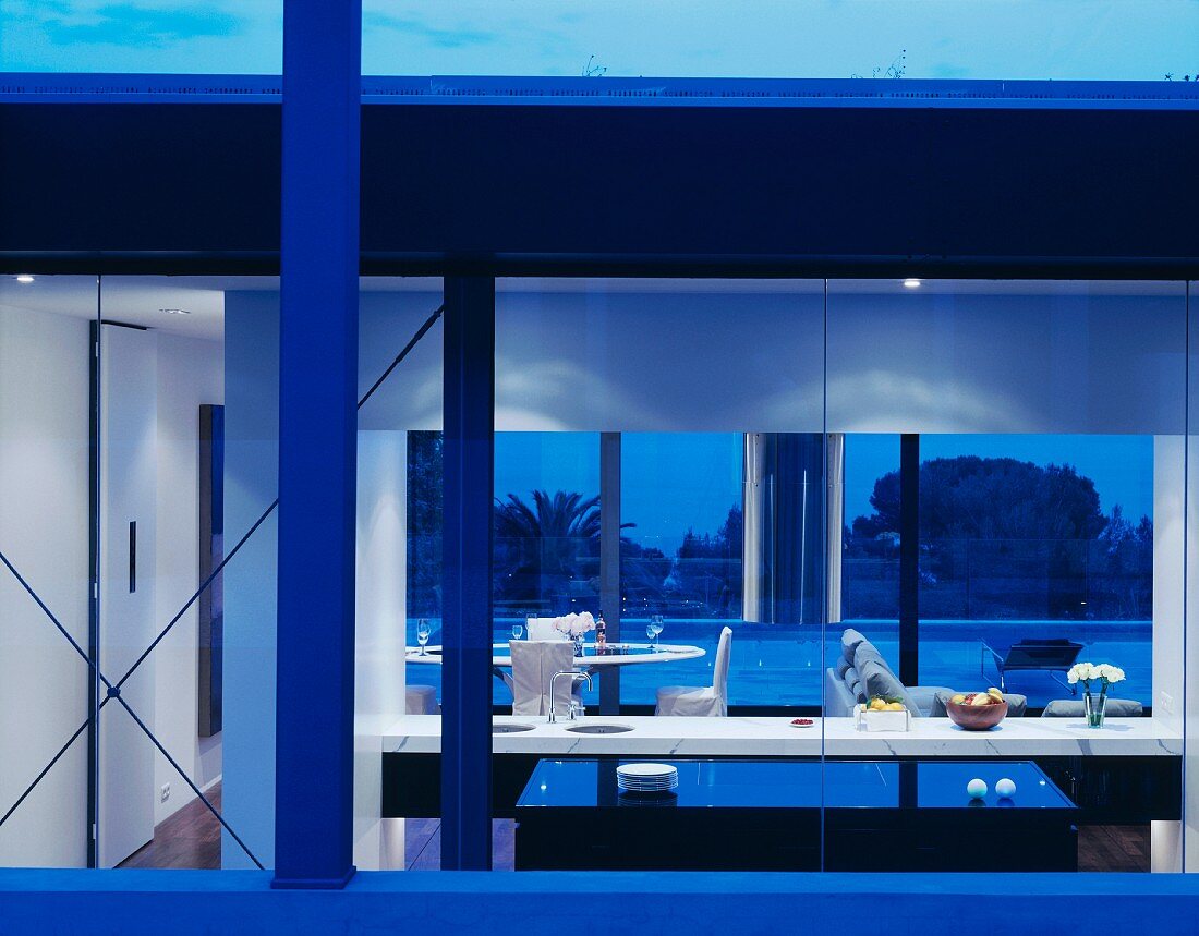 Zeitgenössisches Wohnhaus in Abendstimmung und Blick durch Glasfassade in beleuchtete offene Küche