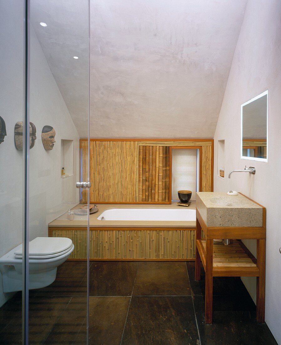 Blick durch offene Glastür in modernes Bad mit Bambusverkleidung an Badewannenfront und braun marmorierten Steinfliesen