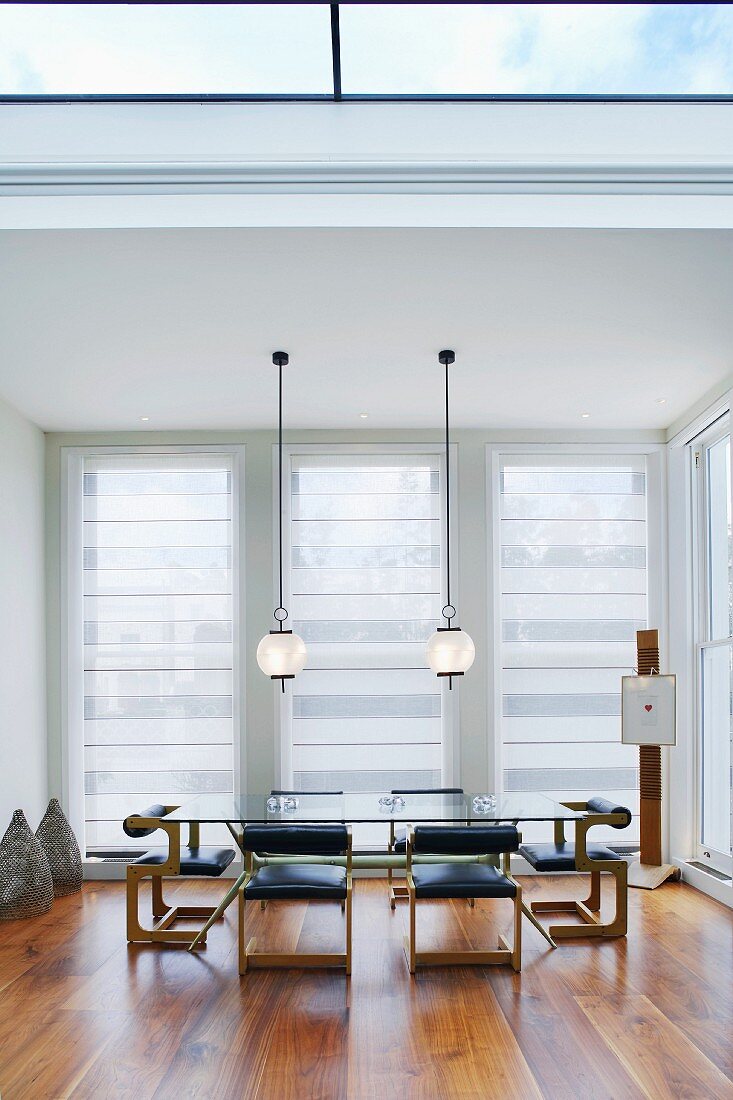 Modern living space with skylight and pendant lamps above dining table and retro leather chairs