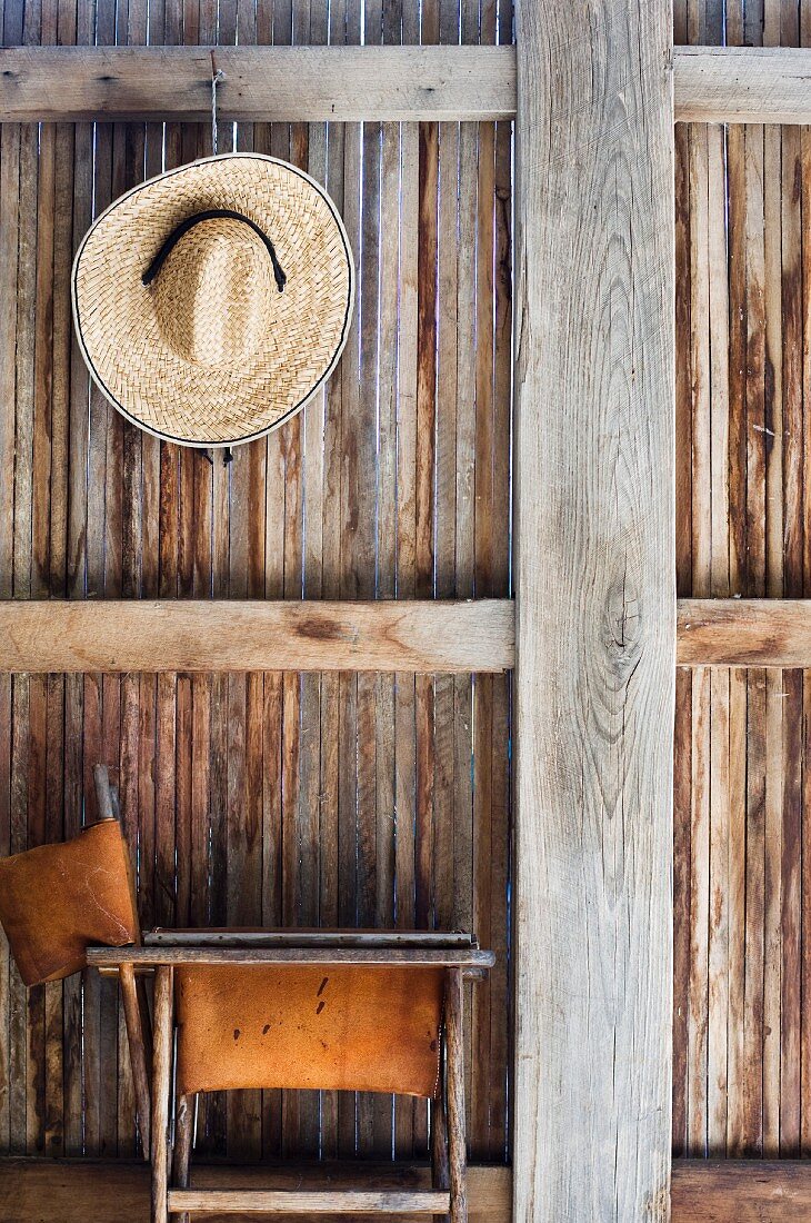 Ein Strohhut und ein alter Klappstuhl vor einer Holzwand