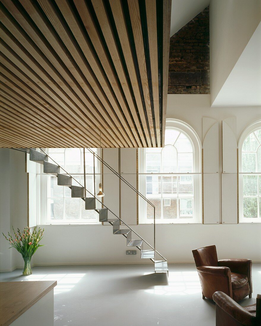 Wohnraum in Villa mit Ledersesseln unter Galerie und leichte Metalltreppe vor Rundbogenfenstern