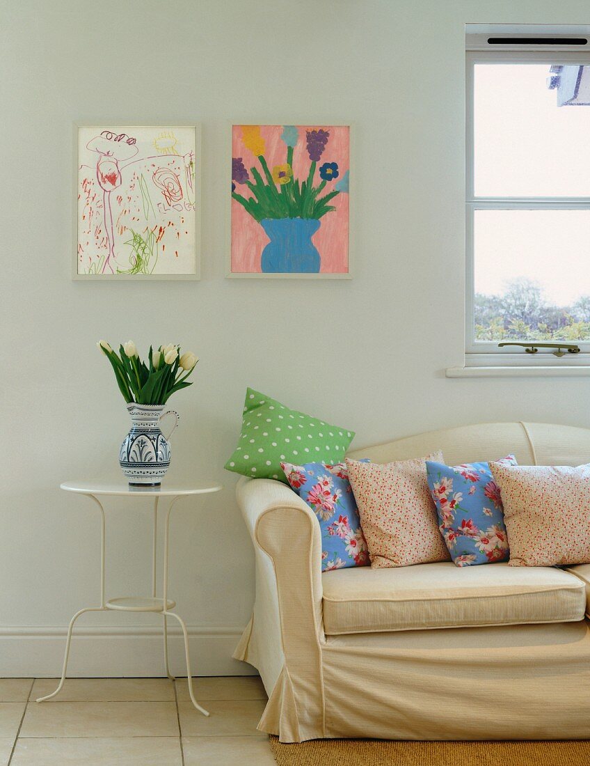 Light upholstered sofa with cushions in front of children's pictures on wall