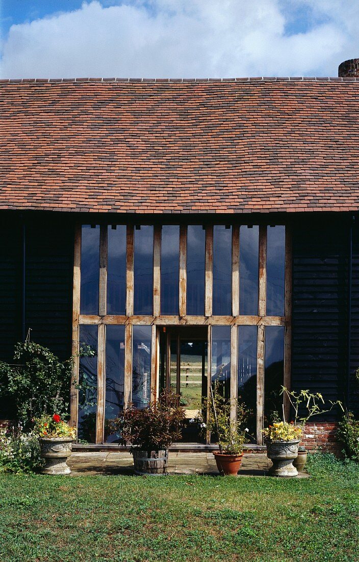 Planters on edge of terrace in front of roof-high windows and tiled roof