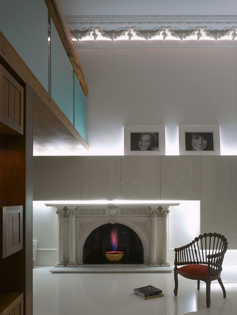 Armlehnstuhl vor weißem massgefertigten Schrank über Kamin und indirekt beleuchteter Stuckfries an Decke eines luxuriösem Wohnraumes