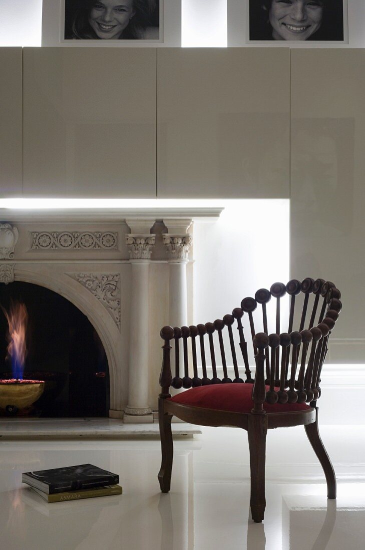 Armchair made from wooden rods topped by spheres on glossy white floor in front of fireplace