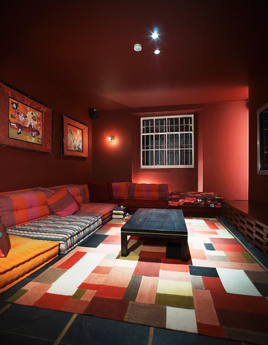 Rotgetönter Raum mit verschiedenfarbigen Sitzpolstern und Patchworkteppich auf Boden