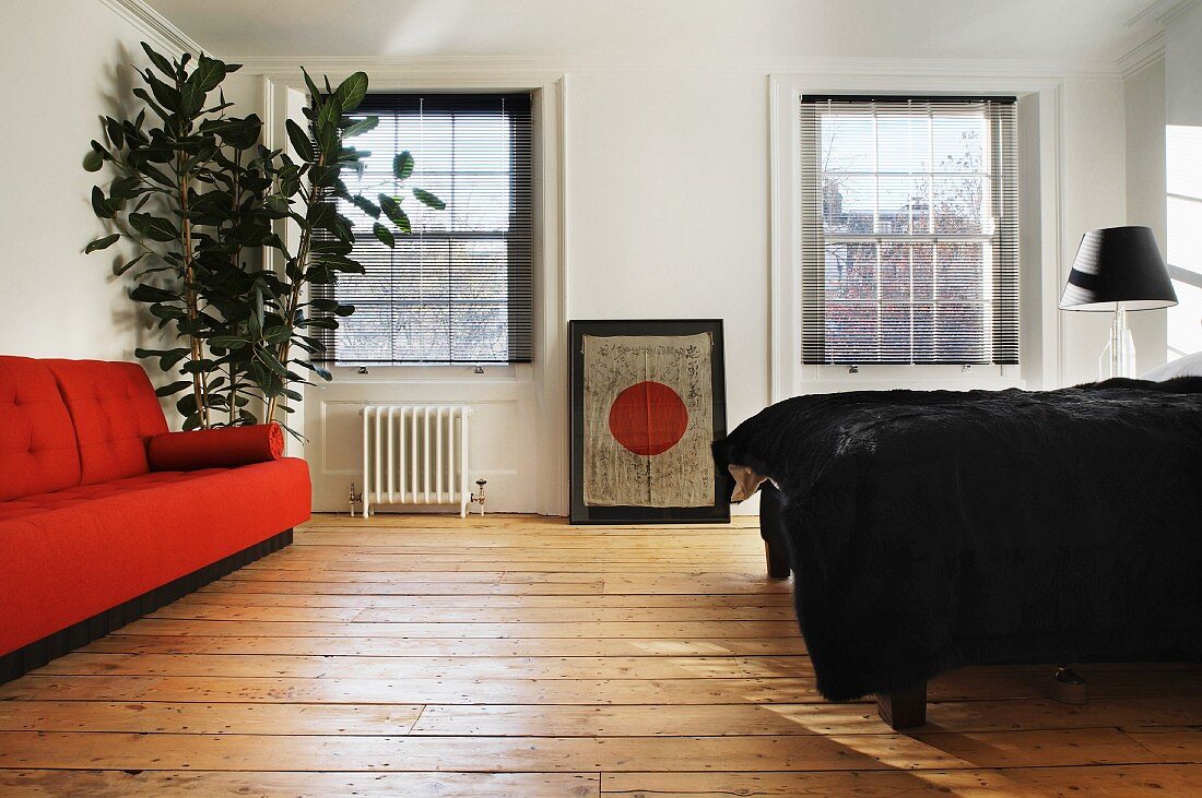 Oranges Sofa und Bett mit schwarzer Tagesdecke auf rustikalem Dielenboden
