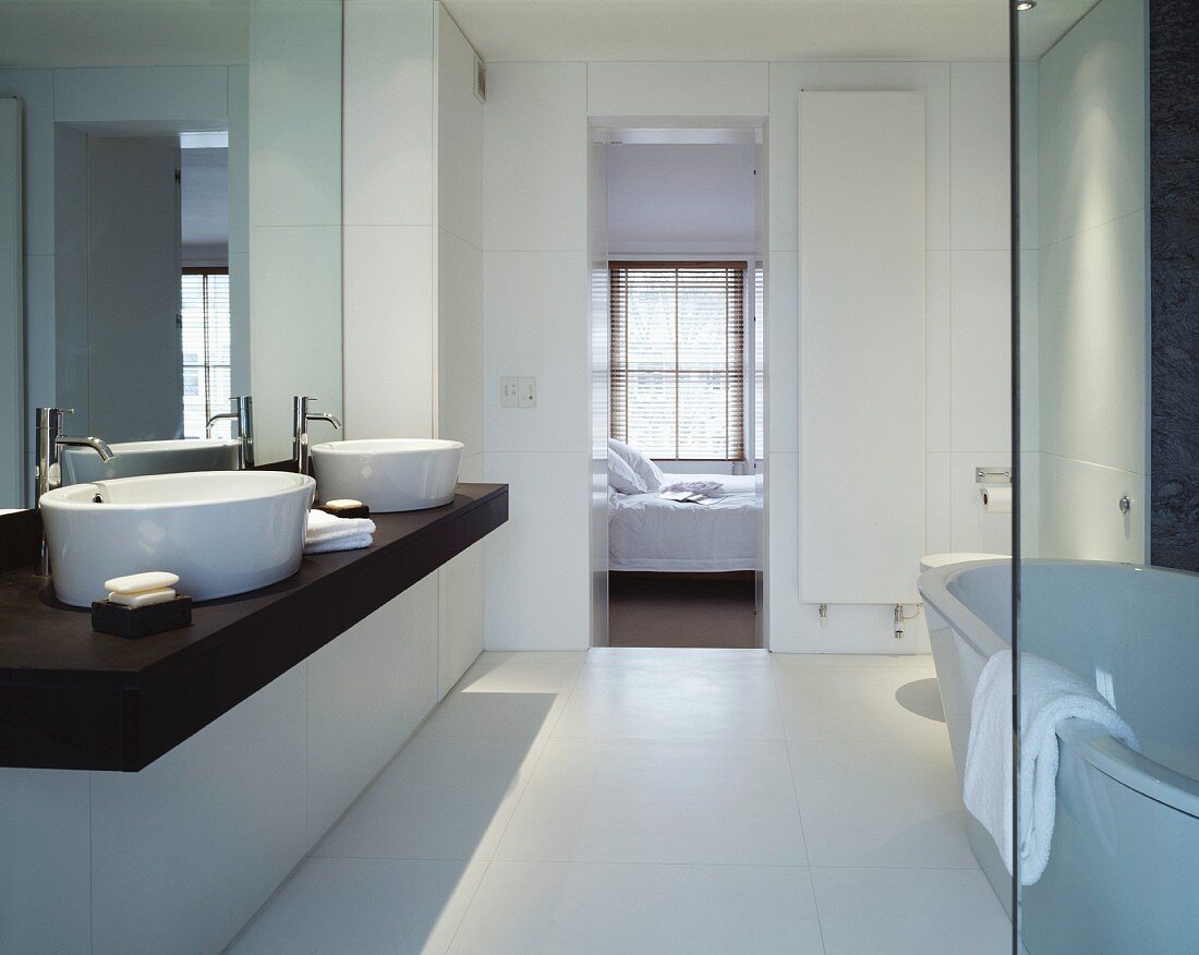 Modern bathroom with two white ceramic sinks on dark wooden counter and view through open bedroom door