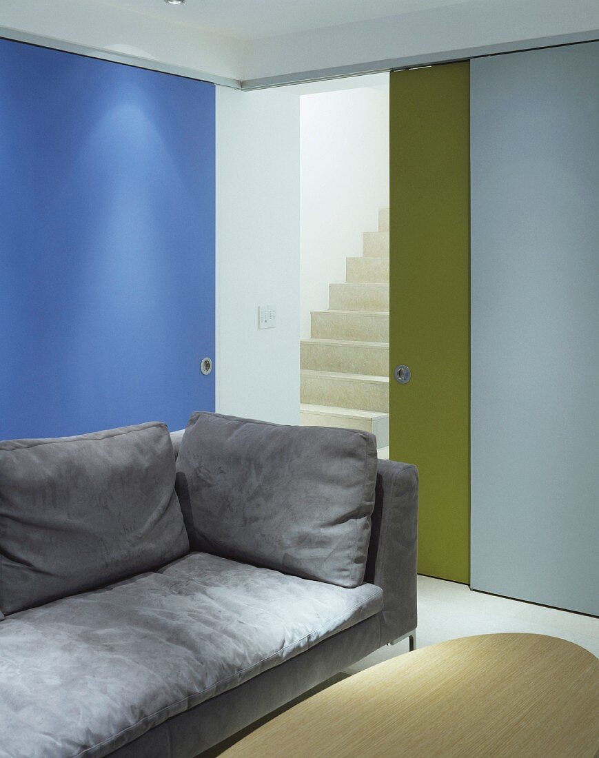 Hellgraues Sofa vor farbigen teils offenen Schiebetüren mit Blick auf Treppe