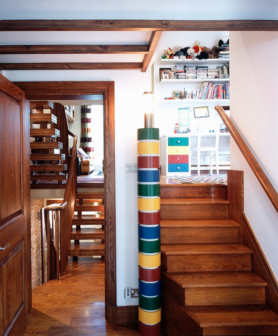 Buntes Säulen-Leuchtobjekt zwischen Holzstufen zu Kinderzimmer und Blick auf zweiläufige Holztreppe