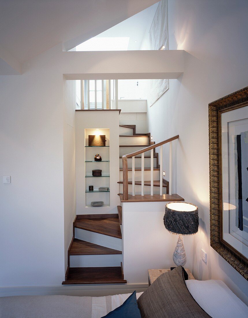 Schlafzimmer mit Zugang zu Bad ensuite über verwinkelte, kleine Holztreppe mit Deko-Regal in beleuchteter Mauernische