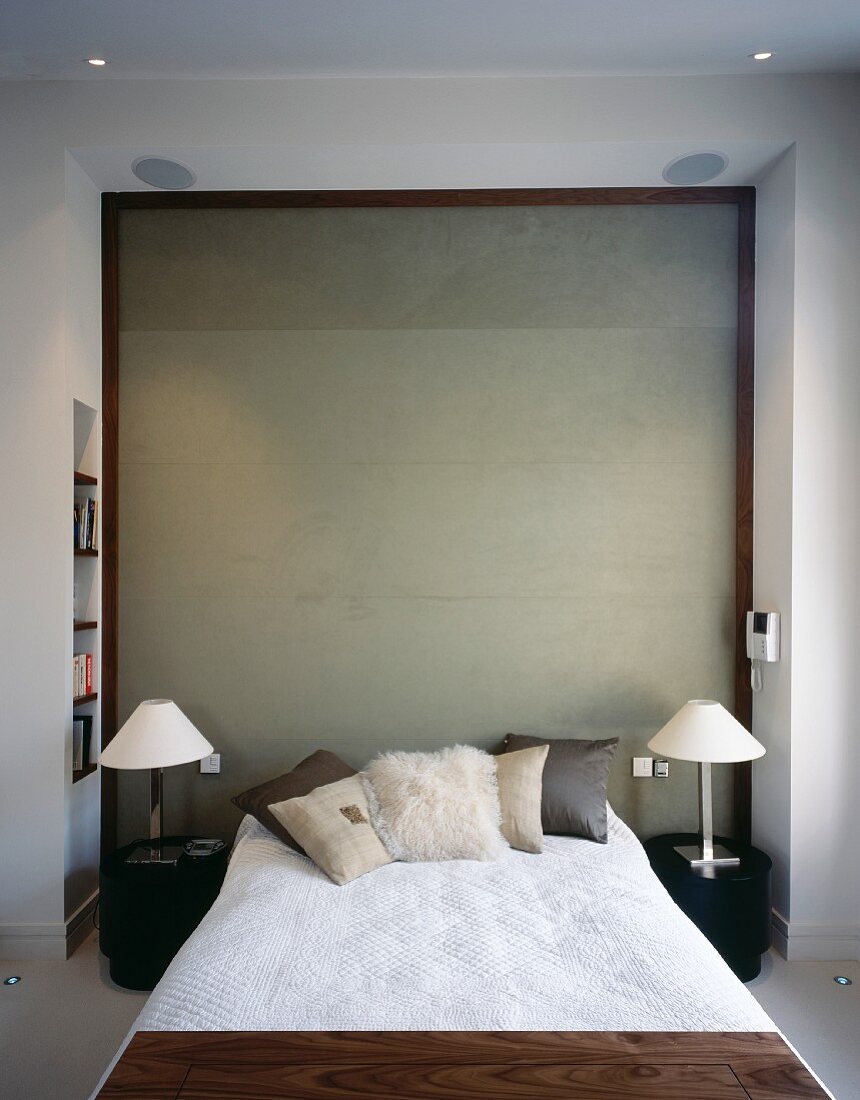 Französisches Bett vor holzgerahmter Sichtbetonwand und moderne Nachttischlampen mit Metallfuss