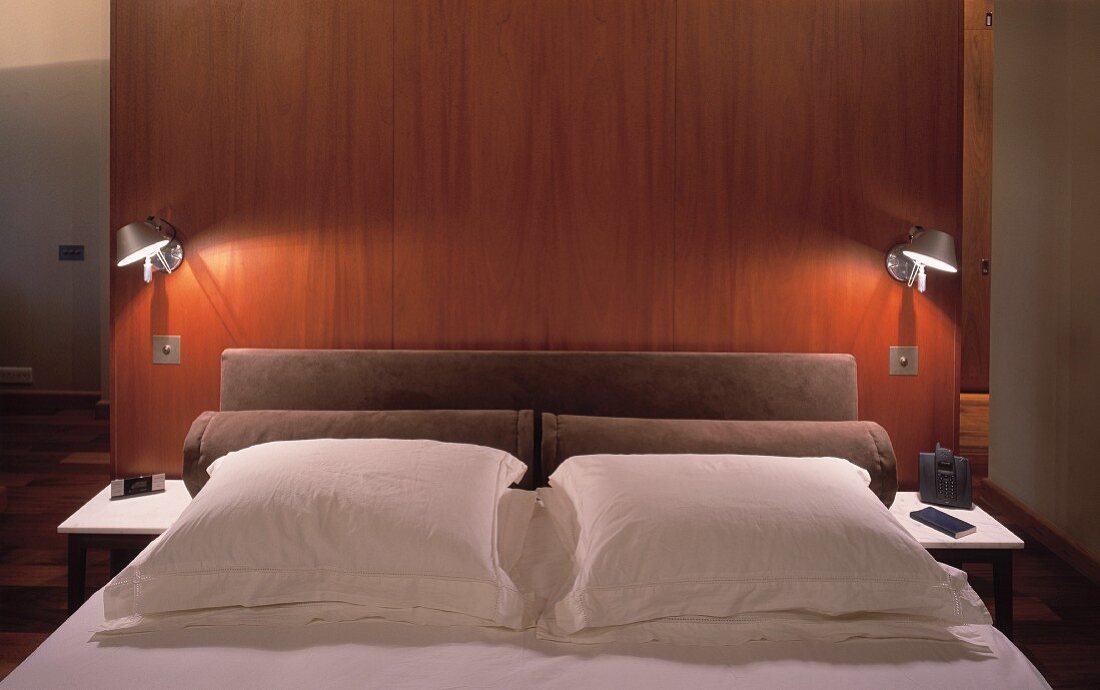 Modernes Doppelbett mit brennenden Wandlampen an freistehender Holzrückwand