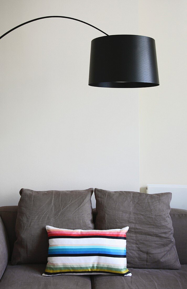 Bogenlampe mit schwarzem Schirm über hellgrauem Sofa mit Kissen