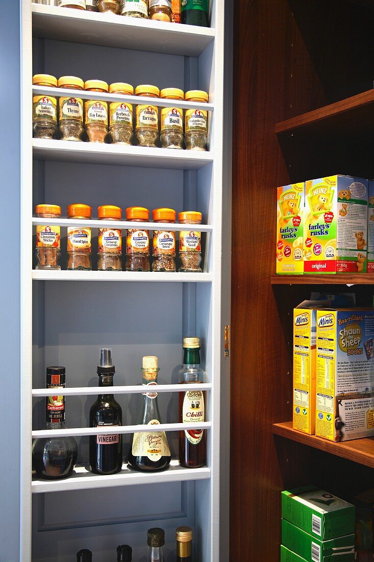 A white spice rack in a niche next to an open shelf stacked with food