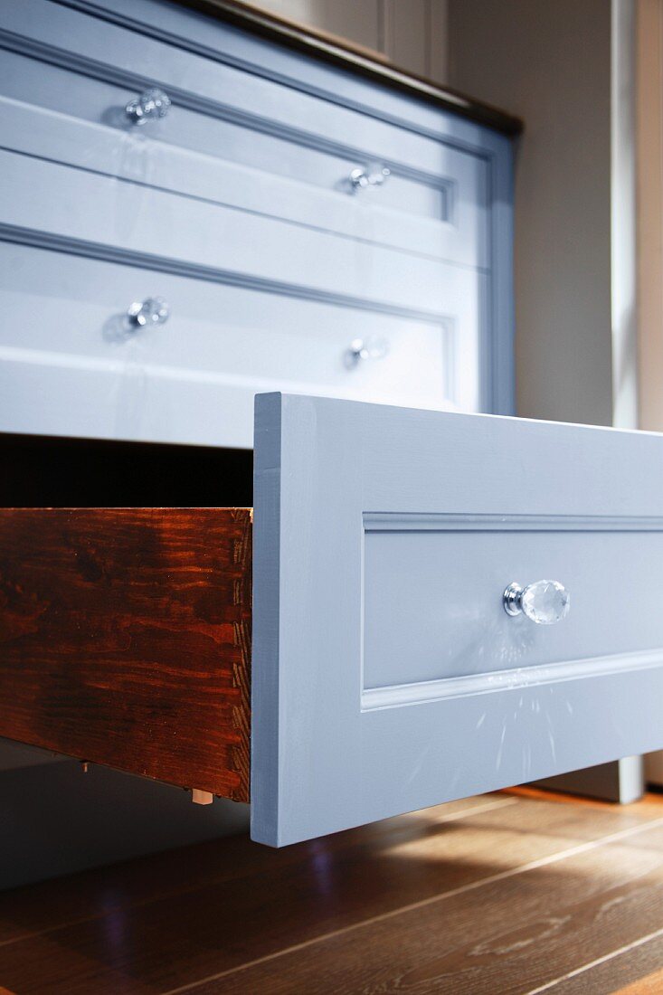 An open drawer in a kitchen cupboard with a shiny, painted front