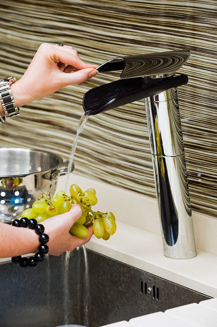 Hand holding grapes under running water from designer tap fitting
