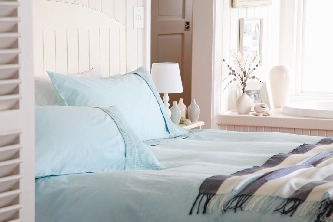 Doppelbett mit hellblauen Kopfkissen und Tagesdecke am Fenster