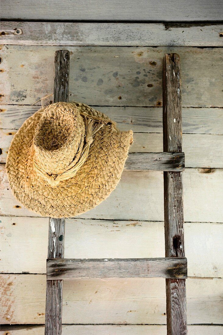 Ladder with straw hat leaning on wooden wall