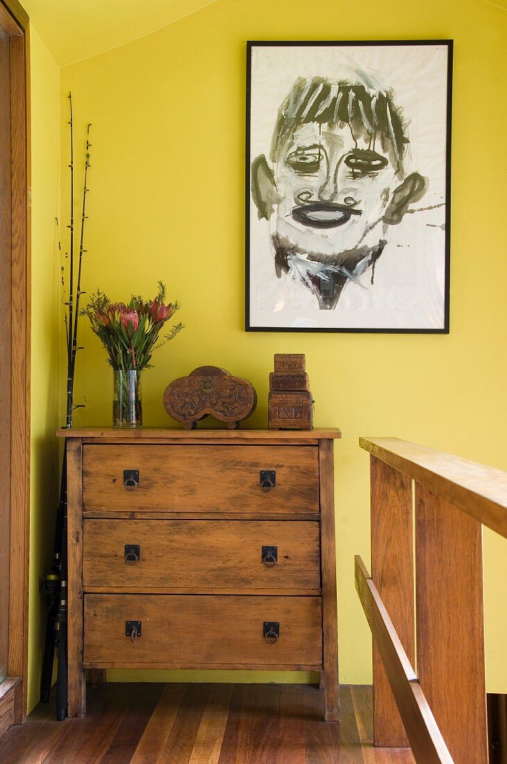 Abstraktes Portrait hängt an der gelben Wand über einer Kommode