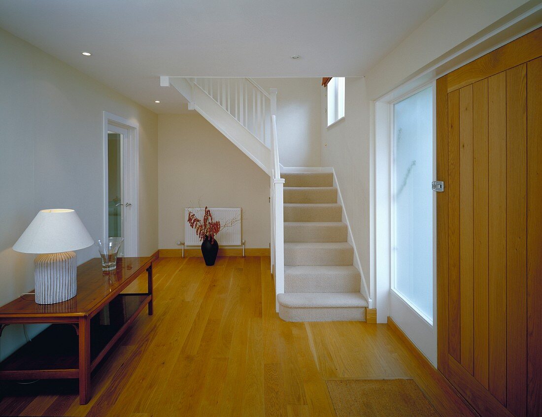 Generous foyer with table lamp on sideboard and white painted wooden stairs
