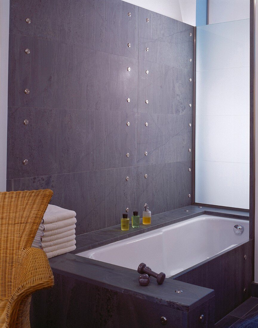 Graue Steinverkleidung mit Edelstahlverschraubung an Wand und Badewanne im Designerstil